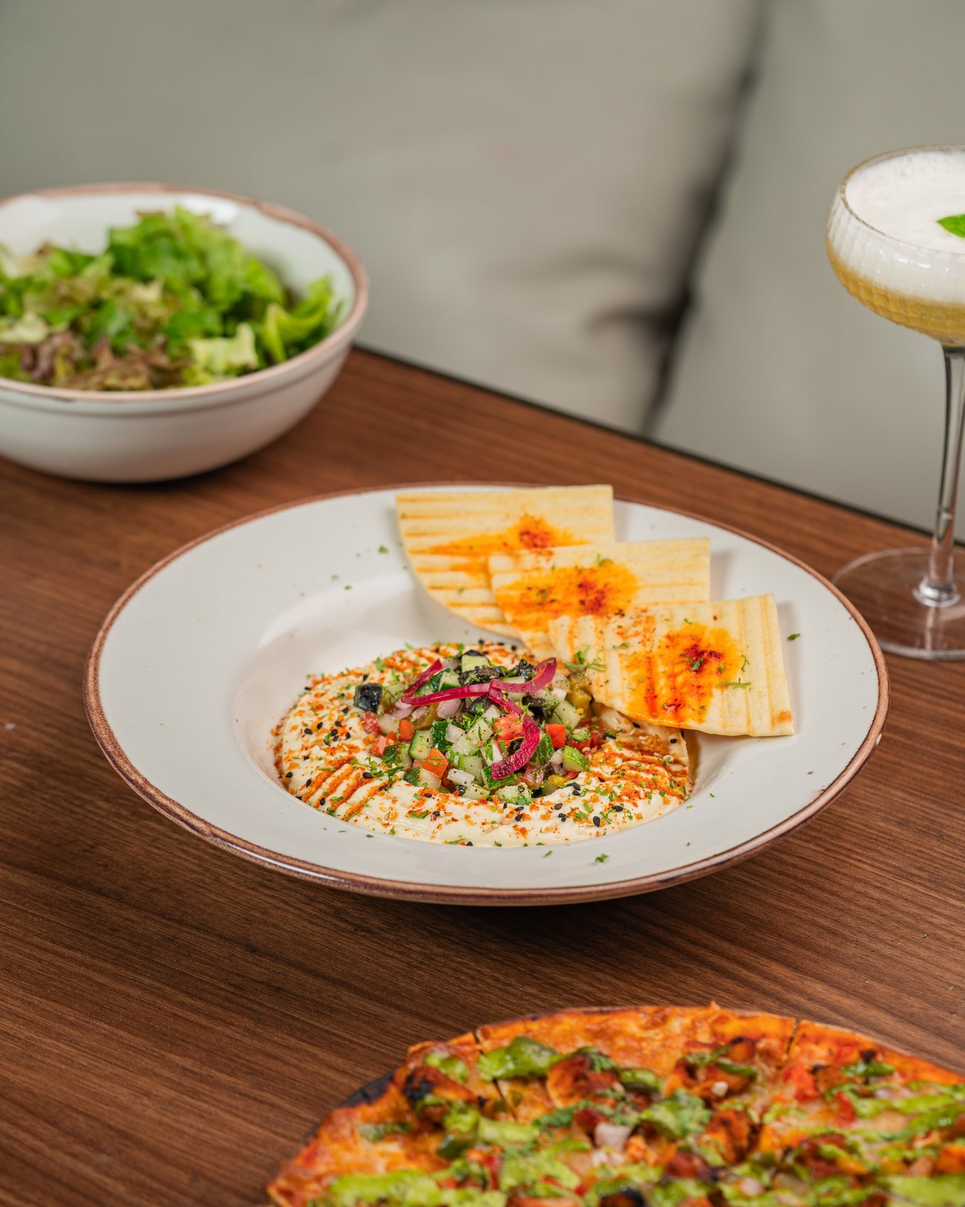 Hummus with flatbread, pizza, salad and a cocktail on a wooden table